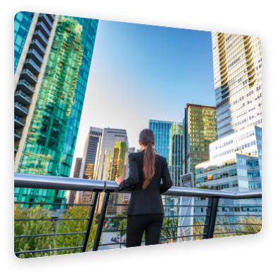 Businesswoman standing on a balcony overlooking a cityscape with modern skyscrapers and greenery.